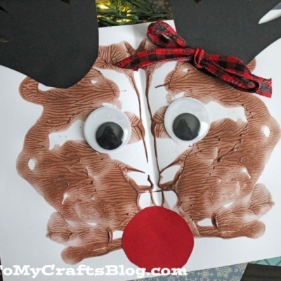 A paint splat reindeer craft made by folding paper with brown paint for the face, large googly eyes, black paper antlers, and a red paper nose.