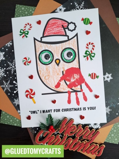 Create a handprint Christmas owl craft featuring a festive owl with a Santa hat, googly eyes, and a red handprint wing. Surrounded by candy and heart stickers, snowflake paper, and a “Merry Christmas” sign. @GLUEDTOMYCRAFTS.
