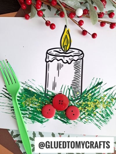 A drawing of a lit Christmas candle on white paper, with grass-like green paint applied using a fork, three red buttons, a green plastic fork, and decorative berries. @GLUEDTOMYCRAFTS is written at the bottom.