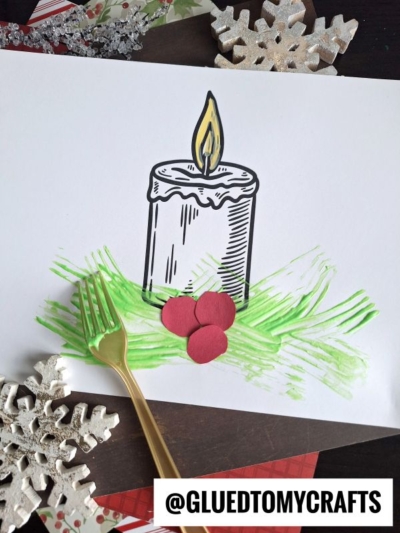 A fork painted Christmas candle on white paper features green paint strokes made with a plastic fork, red paper circles as berries, and decorative snowflakes; @GLUEDTOMYCRAFTS is written at the bottom.