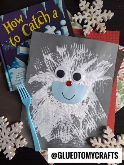 A children’s craft featuring a fork painted white yeti with large googly eyes, a blue face, and a red nose on gray paper, shown with a blue fork, book, snowflakes, and the @GLUEDTOMYCRAFTS label.