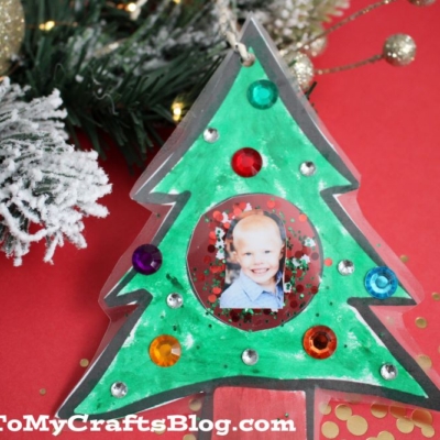 A handmade Holiday Tree Photo Ornament crafted from paper and colorful gems, featuring a child’s photo in the center.
