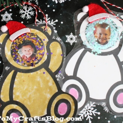 Two Bear Photo Ornaments featuring children's faces, glitter accents, and tiny red Santa hats sit on a black background with white snowflake patterns. The text GluedToMyCraftsBlog.com appears at the bottom.
