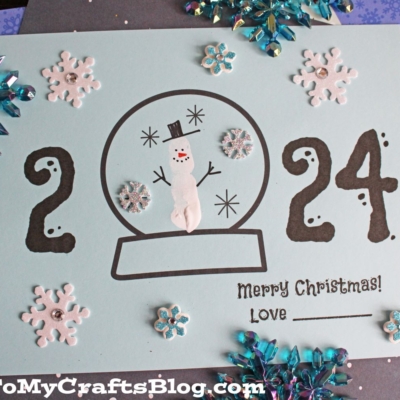 Snowman Christmas Card Craft Idea For Kids - A handmade Christmas card with a snow globe design, snowflakes, and the date 2024