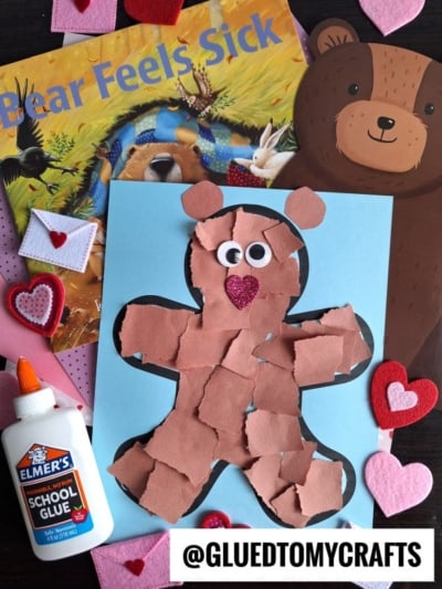 A torn paper bear craft made from brown paper on blue is surrounded by a bottle of glue, the “Bear Feels Sick” book, felt hearts, and bear decorations. The @GLUEDTOMYCRAFTS handle is shown at the bottom.