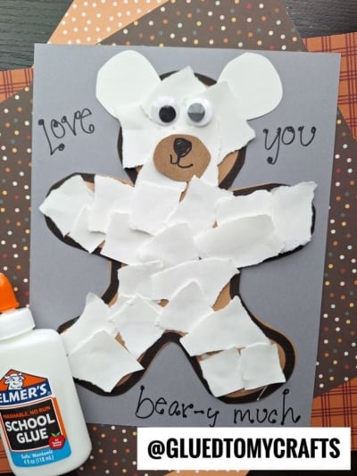 A torn paper bear is made by gluing pieces of white paper onto a bear outline on gray paper, finished with googly eyes and “Love you bear-y much” written around it. Elmer’s school glue and patterned paper are also shown.