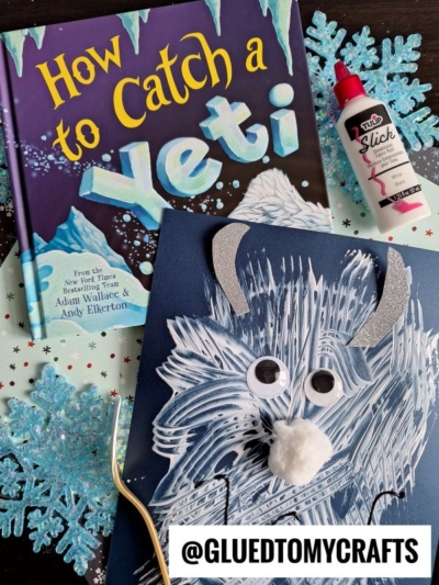 A children's book titled How to Catch a Yeti is next to a winter-themed craft featuring a fork painted yeti made with white and blue paint, googly eyes, and a pom-pom nose on dark paper, surrounded by snowflakes and craft supplies.