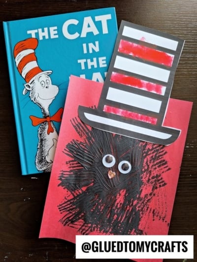 A copy of The Cat in the Hat book sits beside a red craft paper with a fork painted cat face, googly eyes, and a striped paper hat. The Instagram handle @GLUEDTOMYCRAFTS appears at the bottom.