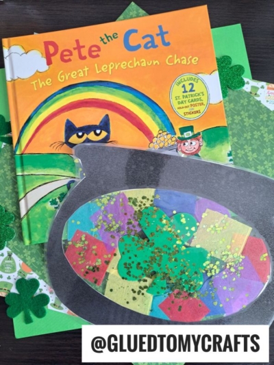 A children’s book titled Pete the Cat: The Great Leprechaun Chase sits on green paper with shamrocks and a sparkling leprechaun cauldron suncatcher craft made of colorful tissue paper and glitter. The handle @GLUEDTOMYCRAFTS is visible.