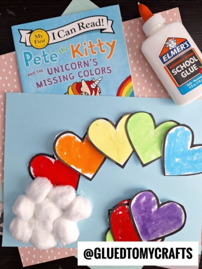 Children’s craft supplies are shown: cut-out colorful paper hearts for a heart rainbow craft, cotton balls, a light blue sheet of paper, Elmer’s School Glue, and a Pete the Kitty children’s book. @GLUEDTOMYCRAFTS is labeled at the bottom.