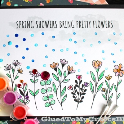 A coloring page with the text Spring showers bring pretty flowers shows hand-drawn flowers, q-tip painted raindrops, paint pots, and cotton swabs arranged around the paper.