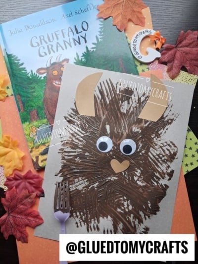 A Gruffalo book and a vibrant fork painted Gruffalo craft with googly eyes are displayed on a table with autumn leaves and colorful paper. A @GLUEDTOMYCRAFTS tag is at the bottom.