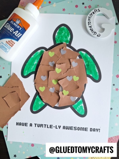 A torn paper turtle craft with a shell made of ripped brown paper and heart stickers on white paper, glue bottle nearby. Text reads HAVE A TURTLE-LY AWESOME DAY! and @GLUEDTOMYCRAFTS.