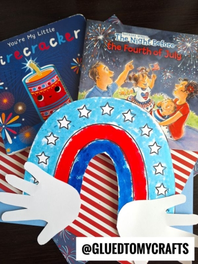 A children’s Fourth of July craft featuring a handprint patriotic rainbow made with a red, white, and blue paper plate, star stickers, hand-shaped cutouts, and two festive books in the background. @GLUEDTOMYCRAFTS text is at the bottom.