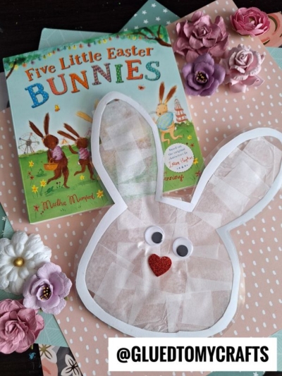 A childrens book titled Five Little Easter Bunnies sits on pastel paper, surrounded by paper flowers, a bunny suncatcher, and a handmade bunny face craft with googly eyes and a red heart nose. @GLUEDTOMYCRAFTS is written at the bottom.