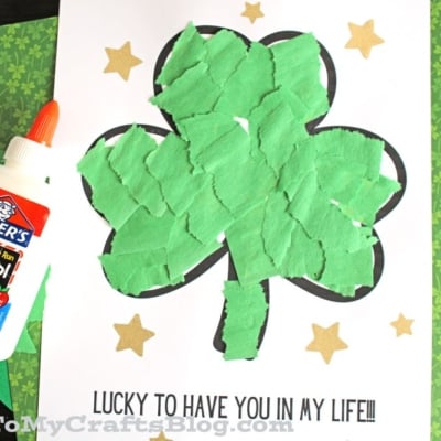A torn paper shamrock outline filled with green pieces sits on a white sheet sprinkled with gold stars. Text reads LUCKY TO HAVE YOU IN MY LIFE!!!