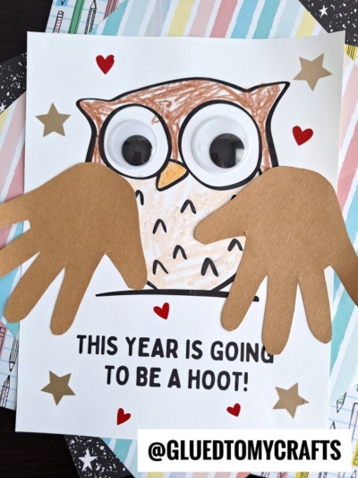 A handprint owl craft with large googly eyes, colored feathers, and the words THIS YEAR IS GOING TO BE A HOOT! on the bottom. Gold stars decorate the page, and a colorful, striped paper creates a cheerful background for this adorable handprint owl.