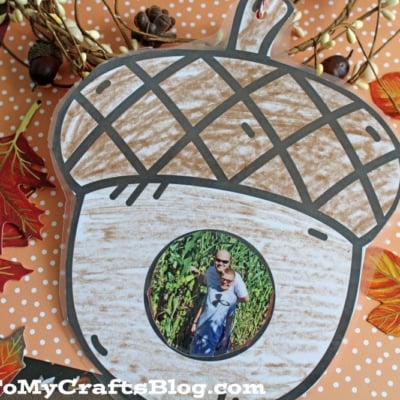 A handmade acorn-shaped Fall Photo Frame Ornament featuring a photo of a man and child, surrounded by autumn leaves and berries on orange, polka-dotted paper. GluedToMyCraftsBlog.com is displayed at the bottom.