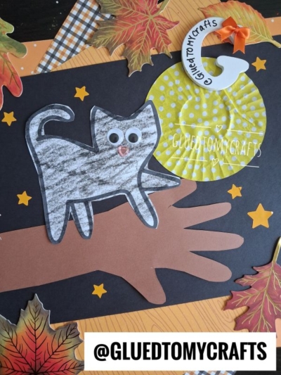A fall-themed craft features a handprint tree with a cat on tree branch, a googly-eyed black cat, yellow stars, paper leaves, and a yellow moon with the text GLUEDTOMYCRAFTS. @GLUEDTOMYCRAFTS label appears at the bottom.