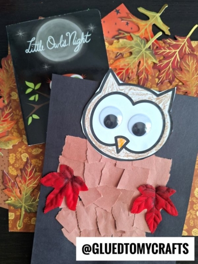 A handmade torn paper owl craft, featuring brown and tan paper pieces, googly eyes, and red leaf decorations, is displayed on a black card. Behind it are a fall-themed book and autumn leaf papers. Text: @GLUEDTOMYCRAFTS.