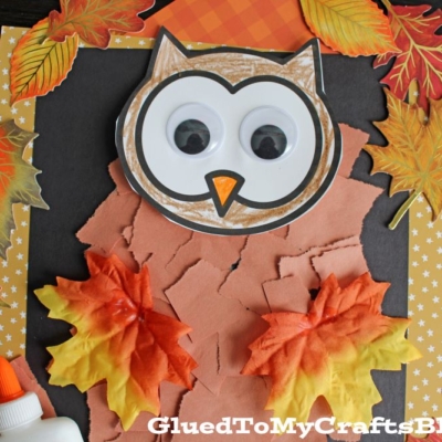 A torn paper owl craft for kids, featuring brown paper, two fake autumn leaves as wings, googly eyes, and a bottle of glue. Set on black paper with a yellow border and scattered leaf designs for a fun, seasonal project.