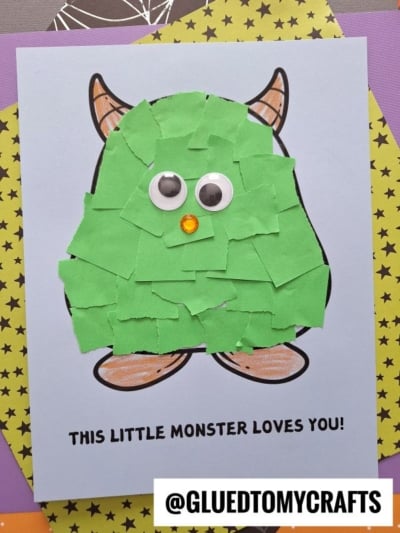 A cute torn paper monster craft made of green paper scraps, two googly eyes, and an orange nose on a card with the text THIS LITTLE MONSTER LOVES YOU! and the handle @GLUETOMYCRAFTS.