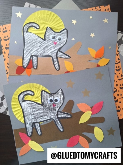 Two paper crafts show a cat on tree branch—gray cats with googly eyes perched on brown branches, surrounded by colorful paper leaves, yellow moons, and gold stars. Halloween-themed paper is used as a background. @GLUEDTOMYCRAFTS is labeled at the bottom.