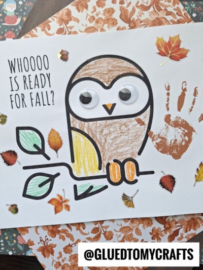 A fall-themed handprint owl craft made with googly eyes, colored leaf stickers, and a handprint for a wing. Text on the paper reads “Whoooo is ready for fall?” @gluedtomycrafts is printed at the bottom.