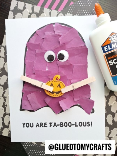A torn paper ghost made from purple scraps, with googly eyes and a clothespin holding a tiny pumpkin cutout. Text below reads YOU ARE FA-BOO-LOUS! Craft glue and patterned paper sit nearby.