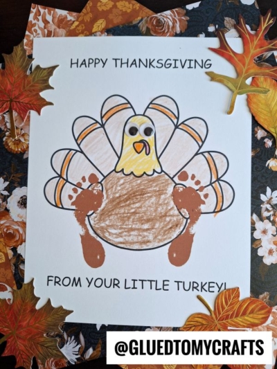 A Thanksgiving craft showing a hand-colored footprint turkey with googly eyes and brown painted handprints as wings, surrounded by autumn leaves and floral paper. Text reads: Happy Thanksgiving from your little turkey!.