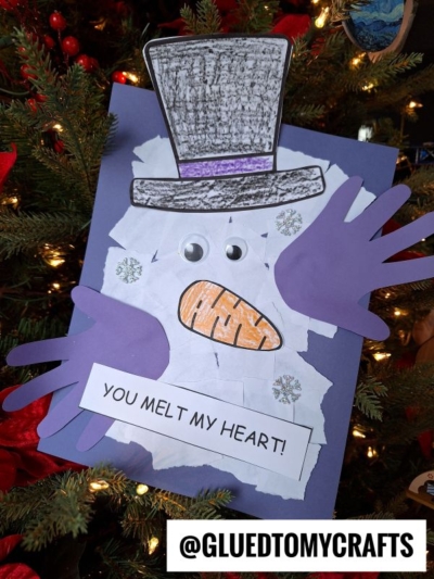 A handmade torn paper melted snowman craft with a white paper body, purple handprint arms, googly eyes, orange nose, gray hat, and “YOU MELT MY HEART!” on a blue background.