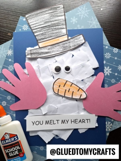 A handmade torn paper melted snowman craft with a paper hat, pink hands, and orange mouth, displayed on snowflake paper with a glue bottle. Text reads YOU MELT MY HEART! and @GLUEDTOMYCRAFTS.