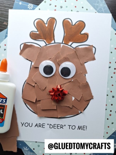 A torn paper reindeer craft featuring big googly eyes, a shiny red bow nose, and a glue bottle beside it. The text reads YOU ARE DEER TO ME! with @GLUEDTOMYCRAFTS at the bottom.
