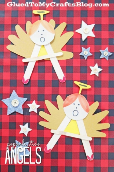 Two popsicle stick angels with paper wings and halos are displayed on a red and black plaid background, surrounded by felt and button stars—an adorable craft that perfectly captures the spirit of “A” is for Angel.