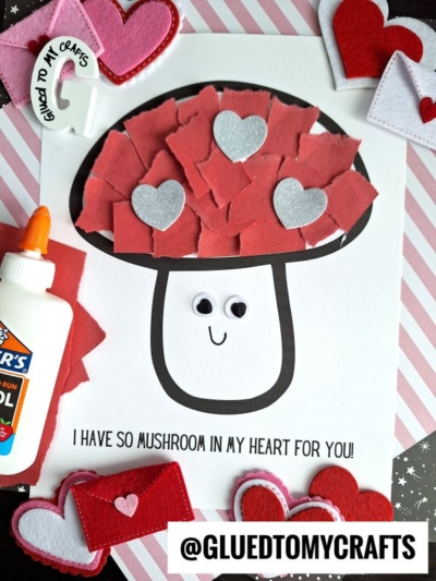 A torn paper mushroom craft made with red and pink pieces, silver heart cutouts, and googly eyes on a worksheet that says I have so mushroom in my heart for you! Surrounded by craft supplies and felt hearts.