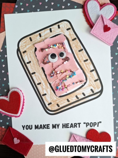 A handmade Valentines Day card features a torn paper pastry with pink frosting, googly eyes, and sprinkles, surrounded by felt hearts and envelopes. Text reads “You make my heart ‘pop!’” and “@GLUEDTOMYCRAFTS.”.