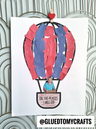 A child’s photo is placed inside a torn paper hot air balloon craft, decorated with red and blue pieces. The balloon features a small red heart on top and the cheerful phrase “Oh, the places I will go!” on the basket.