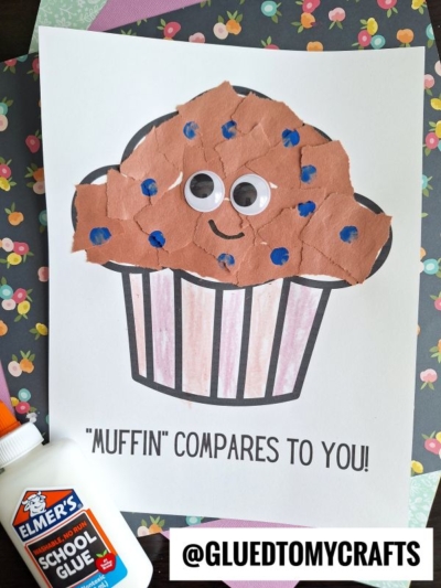 A craft project features a torn paper muffin with brown pieces, googly eyes, blue dots, and a smile on a striped base. The text reads "Muffin compares to you!" with a bottle of Elmer’s glue nearby.