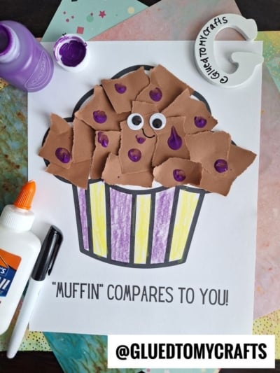 A children’s craft project featuring a torn paper muffin on a colorful background, decorated with brown paper pieces, googly eyes, and purple paint. Text below reads “MUFFIN COMPARES TO YOU!” Craft supplies are nearby.