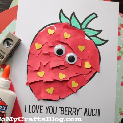 A handmade torn paper strawberry card decorated with red paper pieces, yellow heart shapes, and googly eyes, featuring the text I LOVE YOU BERRY MUCH!