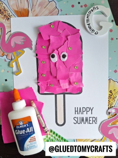 A summer craft project features a torn paper popsicle ice cream bar decorated with pink scraps, googly eyes, and gem stickers, surrounded by craft supplies, flamingo cutouts, and the text HAPPY SUMMER! and @GLUEDTOMYCRAFTS.