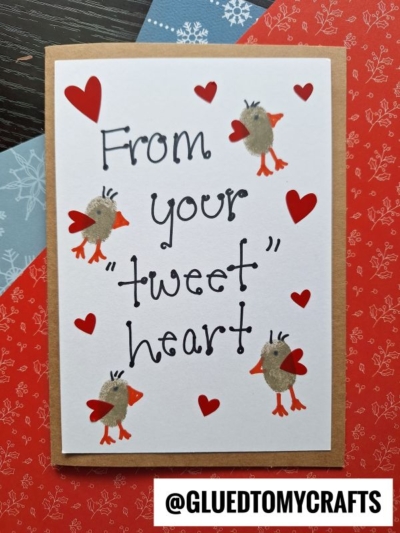 A handmade card with red hearts and four birds made from thumbprint crafts. The card reads From your tweet heart in playful black lettering, with the creator’s handle, @GLUEDTOMYCRAFTS, at the bottom.