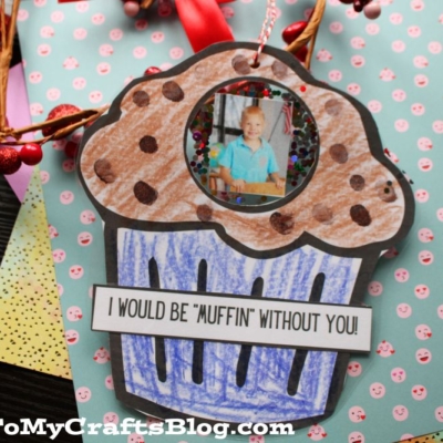 A handmade muffin photo ornament card, colored in brown and blue, displays a child's photo on top. The card reads I WOULD BE MUFFIN WITHOUT YOU! and lies on decorative berry paper.