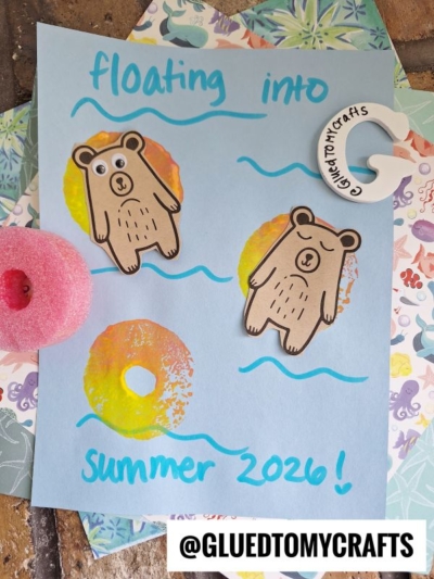 A blue paper with hand-drawn waves, two cartoon bears on pool floats, and text reading floating into summer 2026! This lazy river bear craft features decorative items and the @GLUEDTOMYCRAFTS handle.