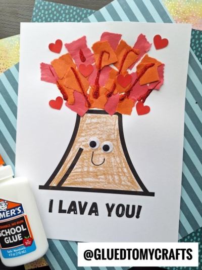 A handmade torn paper volcano craft on paper features orange and red lava, red heart cutouts, googly eyes, and the text I LAVA YOU! at the bottom. Glue and patterned paper add extra decoration to the background.