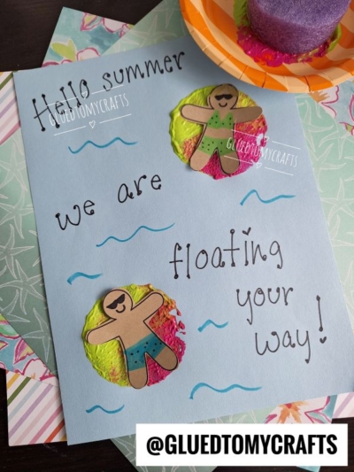 A blue card with Hello summer, we are floating your way! written in black, decorated with paper gingerbread people in swimsuits floating on Pool Noodle Stamped Inflatable Raft sponges. The background features patterned paper.