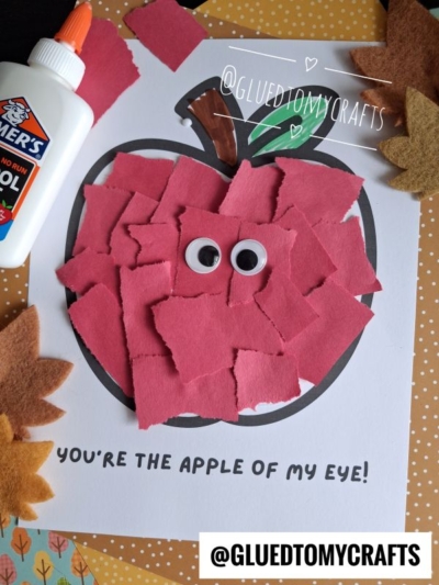 A torn paper apple craft featuring red torn paper, googly eyes, glue, and felt leaves is displayed on a dotted background. The text reads "You’re the apple of my eye!" and @GLUETOMYCRAFTS.