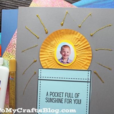 A handmade card displays a child's photo in the center of a yellow sun above a blue pocket, capturing the spirit of "pocket full of sunshine" with gold rays and the text “A POCKET FULL OF SUNSHINE FOR YOU!”