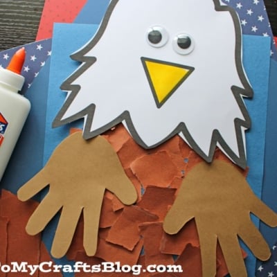 This torn paper eagle craft features a white eagle head with googly eyes, a yellow beak, brown paper handprint wings, and brown torn paper feathers against a blue, red, and star-patterned background.