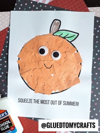 A handmade torn paper orange craft made with orange paper pieces glued inside a drawn circle, featuring large googly eyes, a leaf and stem on white paper. Text below reads “Squeeze the most out of summer!”.